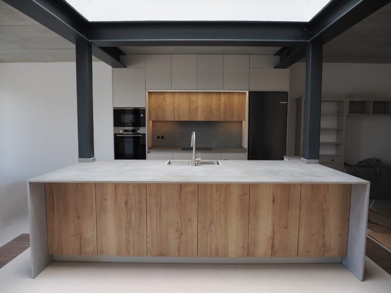 Cocina a medida en Mallorca con isla central, encimera Dekton Soke, acabados Gris Angora y Roble Halifax, iluminación LED cálida y electrodomésticos Bosch en negro.